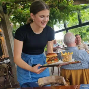 Marij serveert een burgerplate in de serre van restaurant Het Raadsel van de Wadden in Oostmahorn Friesland